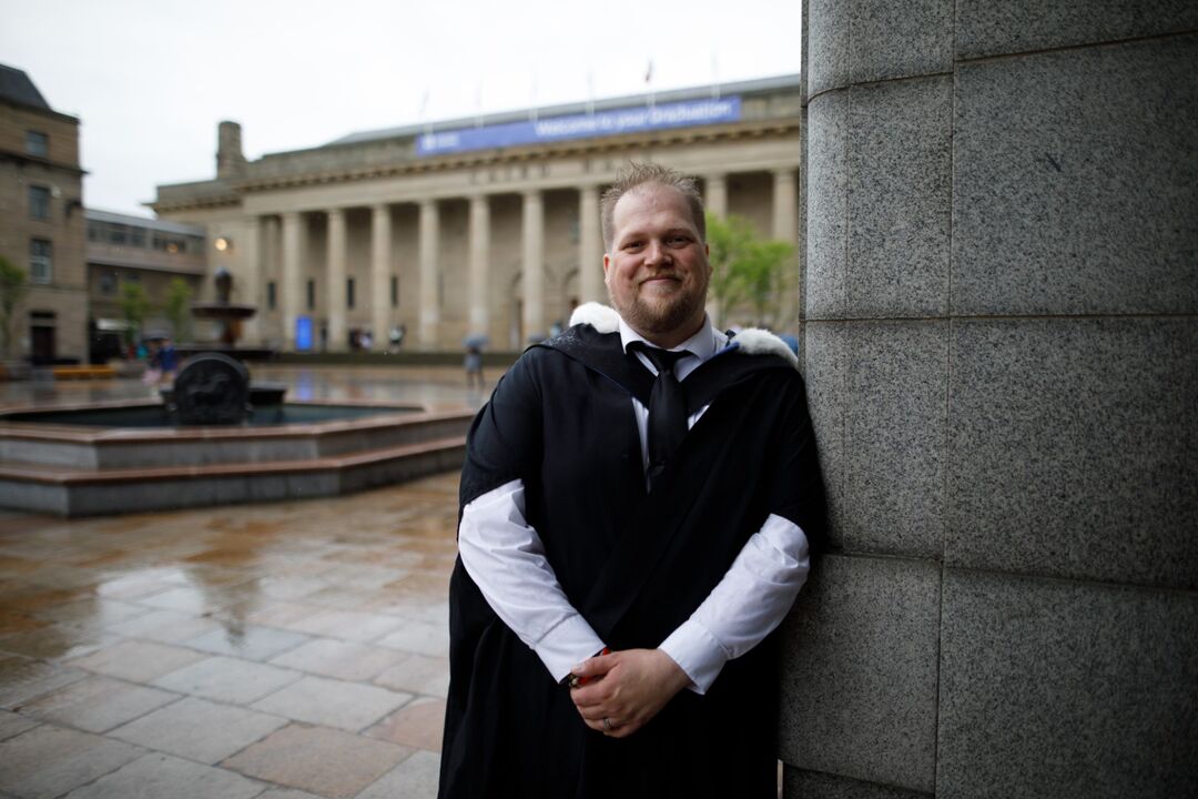 Joe Fordyce in graduation gown stood next to pillar outside caird hall 