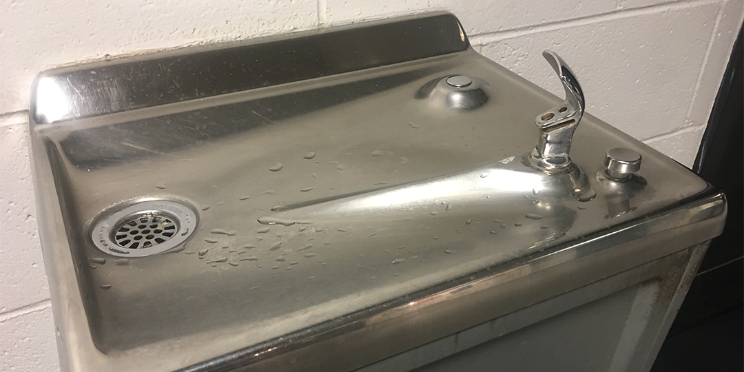 A metal drinking fountain against a white wall