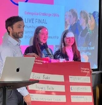 Three people stand holding a large red cheque between them.