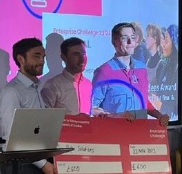 Three people standing in front of a screen holding a large red cheque.