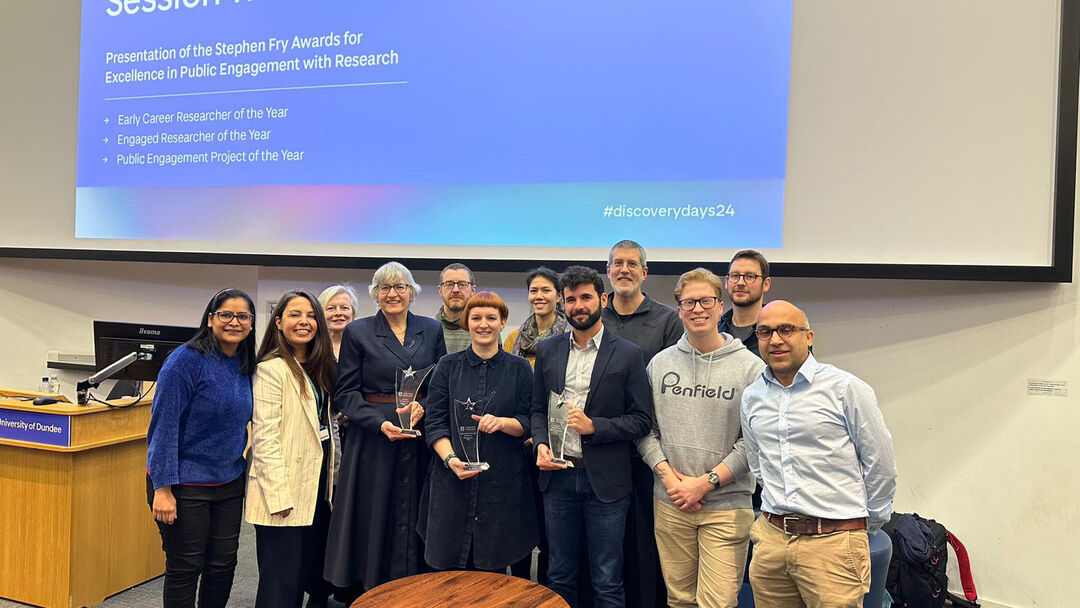 Winners of the 2024 Stephen Fry Public Engagement Awards celebrate, standing in a group at the front of a lecture theatre.