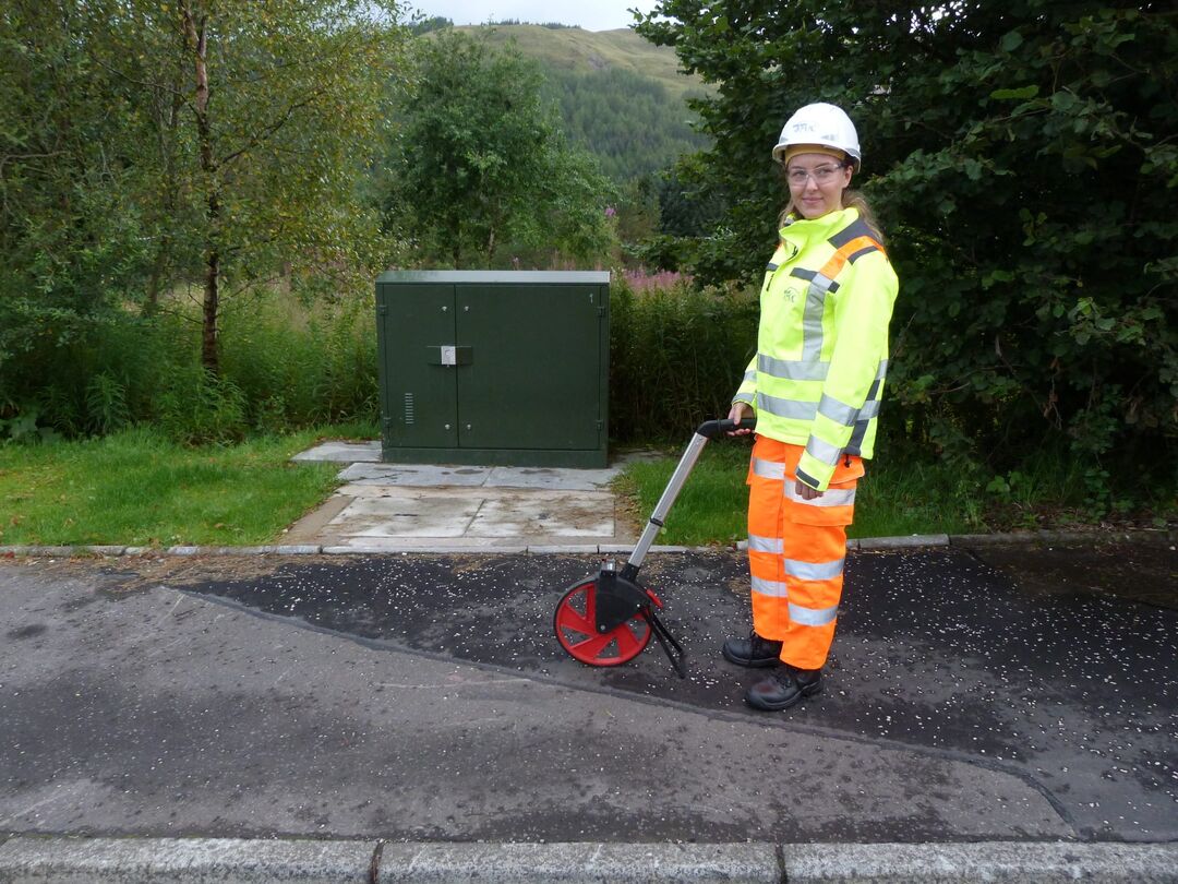 student in fluorescent yellow jacket and hard hat with a measuring device