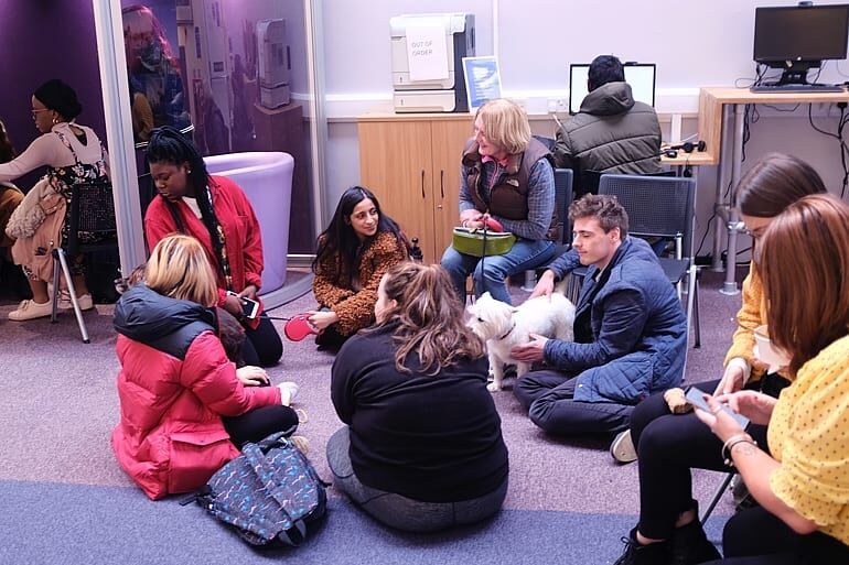 group of students sitting round in circle with small white dog