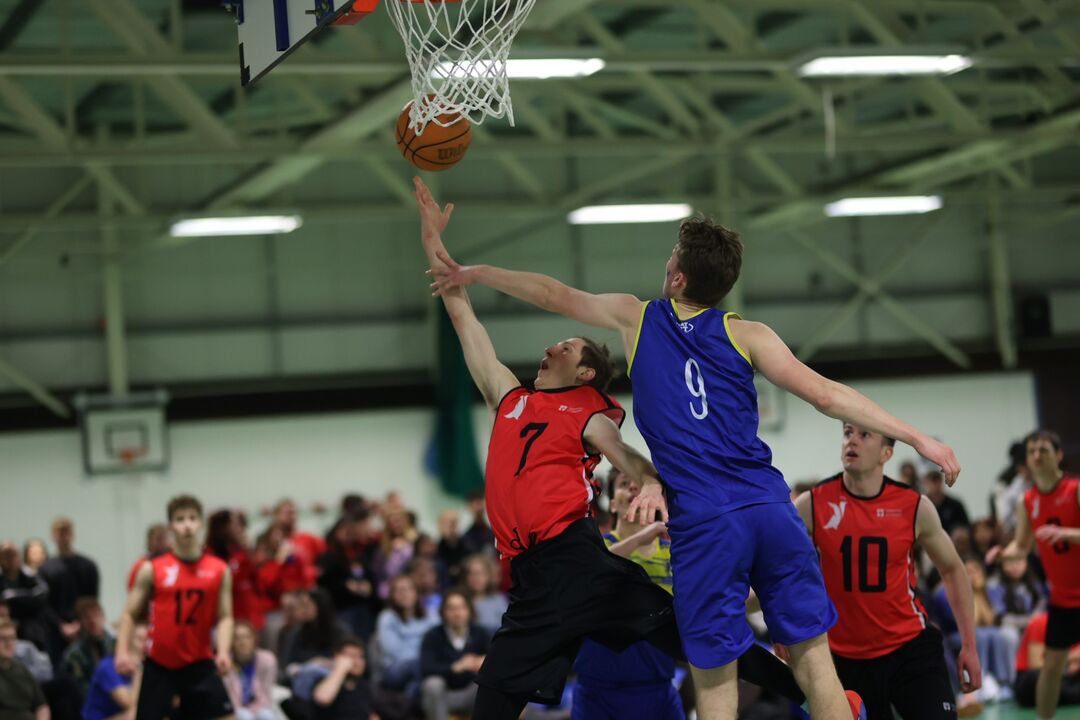 action shot of two teams playing basketball and jumping towards the ball at a goal