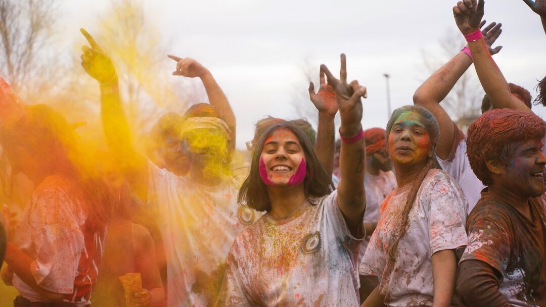 Students at a Holi celebration on Dundee's campus, throwing yellow powder into the air. The students clothing is already marked with colour.