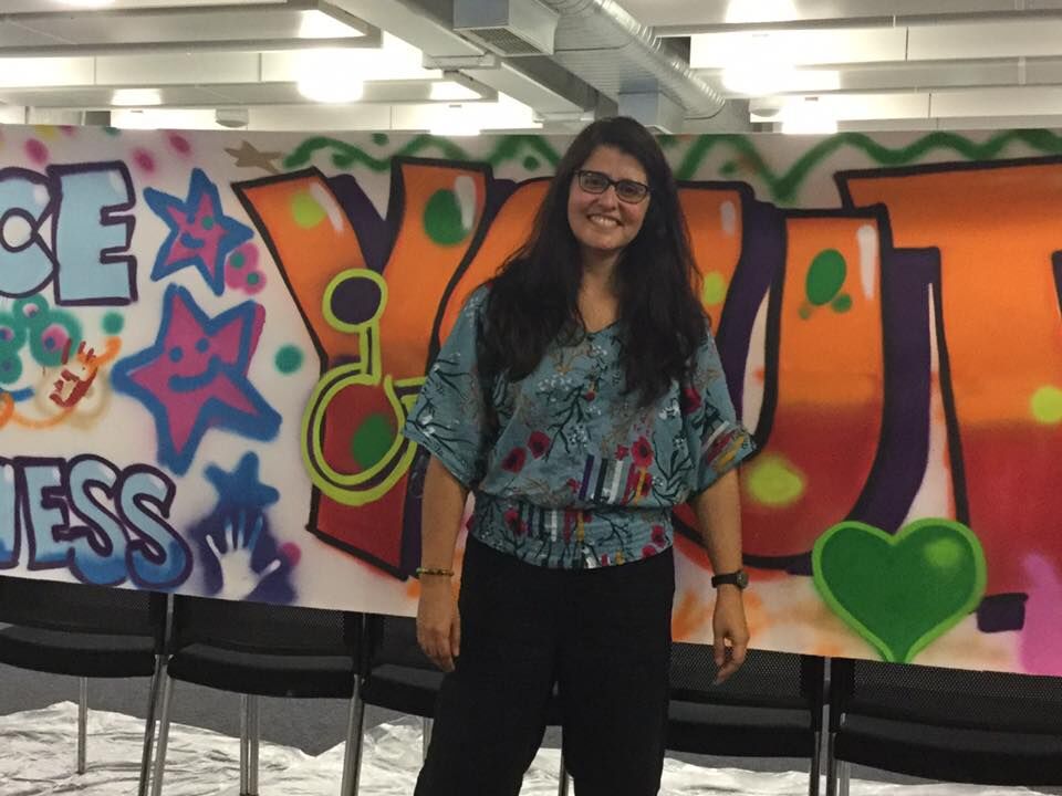 Woman with long dark hair standing in front of a wall with graffiti on it