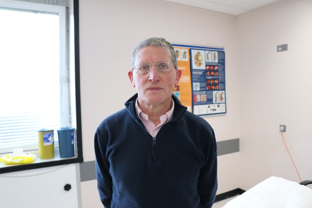 man wearing a dark jumper and glasses looking towards the camera with a straight face