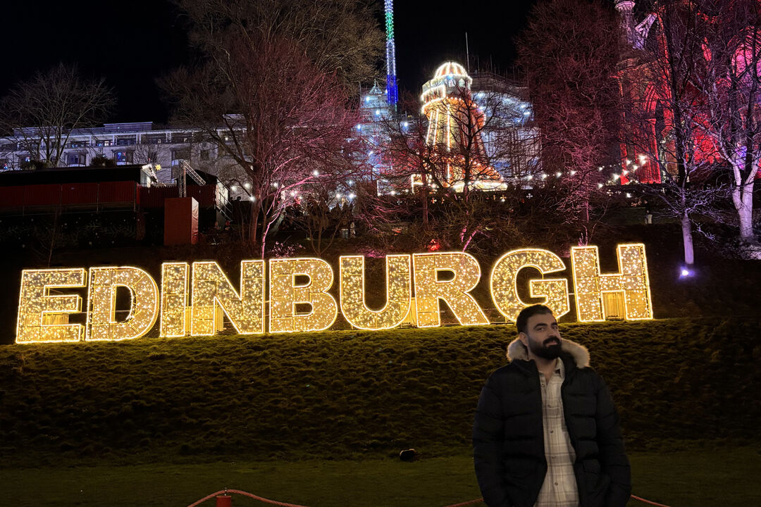Raghav standing in front of a lit up Edinburgh sign