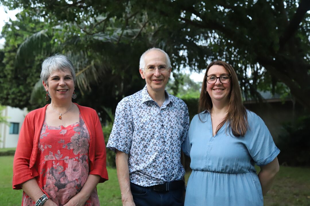 Three people standing next to each other in a garden with trees behind them
