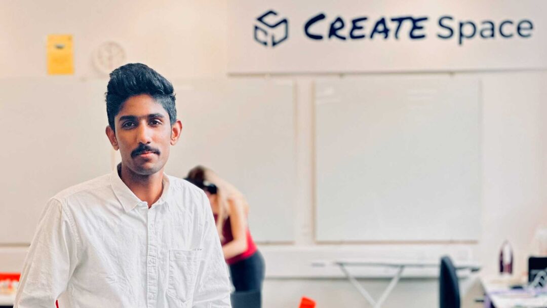 Gokul Raghunathan, wearing a white shirt, standing in a room with large white boards and words "Create space" written on the wall in the background.