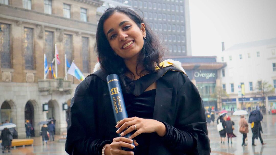 A female on graduation smiling at the camera, in her graduation gown holding a scroll.