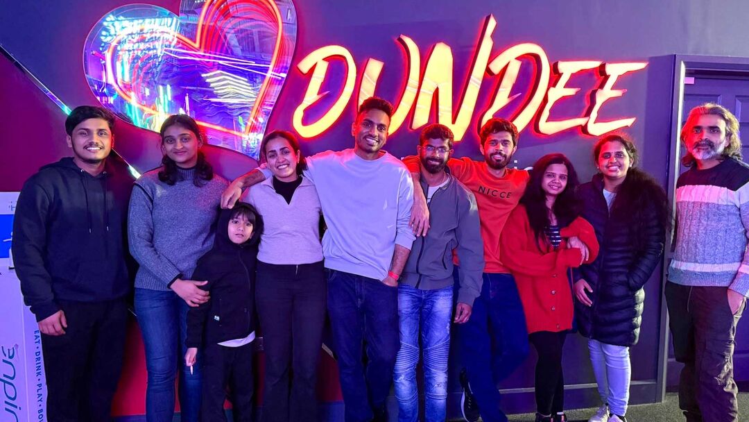 Group of friends posing together infront a Dundee sign that’s lit up.