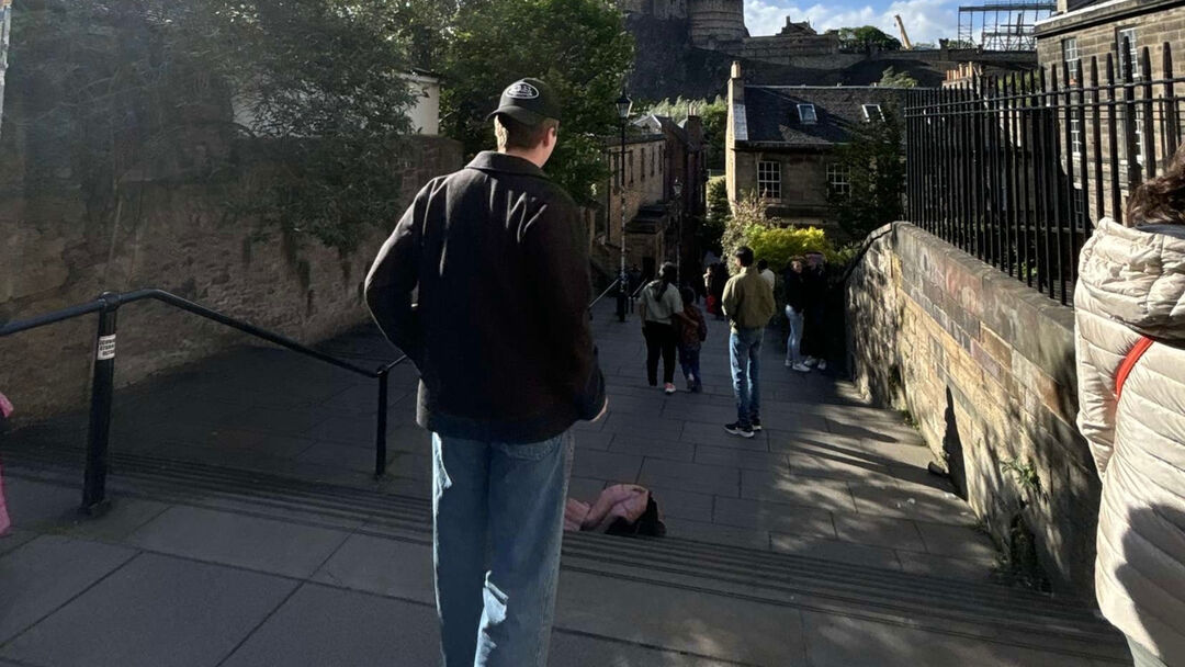 Student walking down a flight of stairs with stone walls and buildings on either side