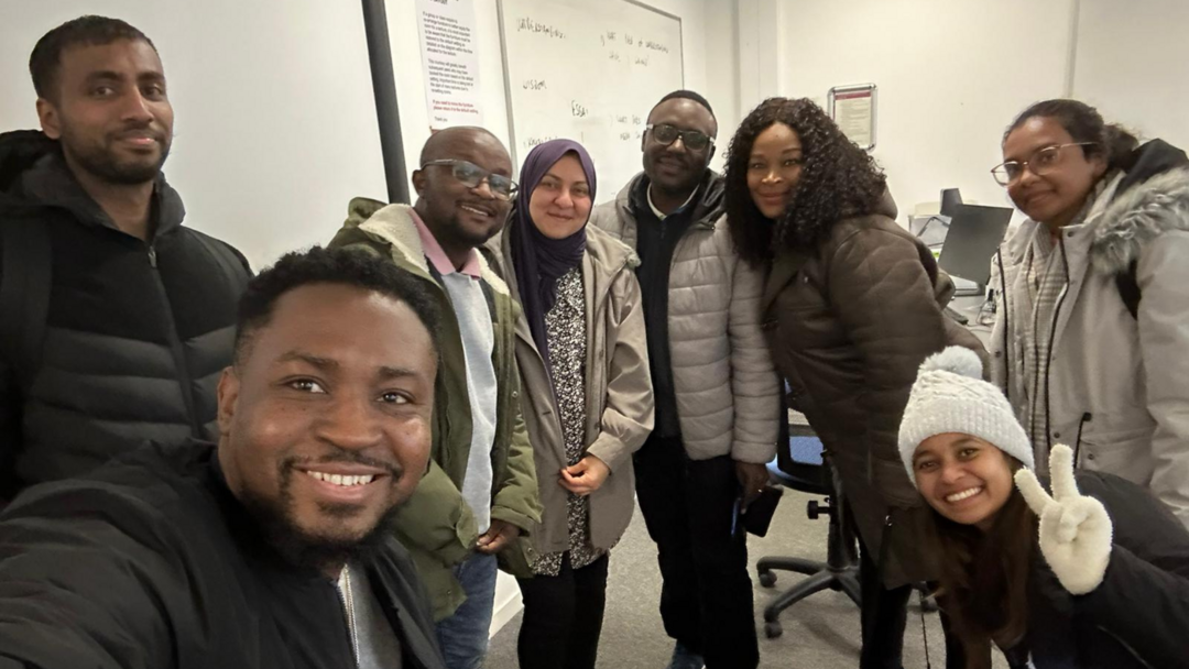 A selfie taking by a student, there are 8 students smiling and posing for the camera, all wearing jackets