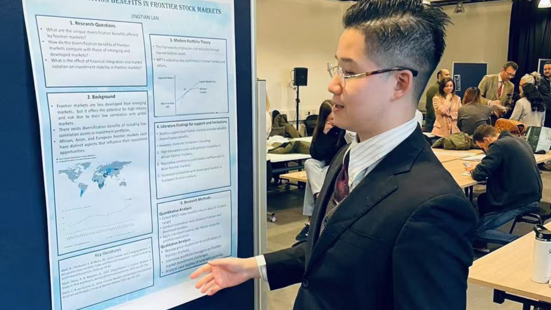 student looking at a project on a board, while wearing a suit and glasses and is turned to to the side, there are other students and academics in the background
