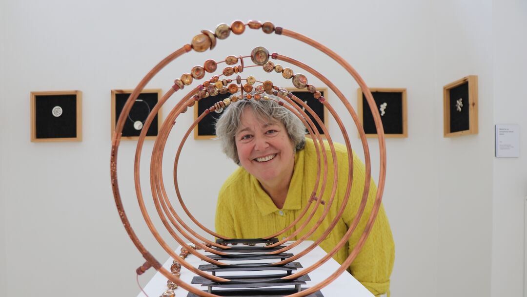 Image looking through a set of copper rings. An older woman wearing a bright yellow shirt is peaking her head through the other side of the rings